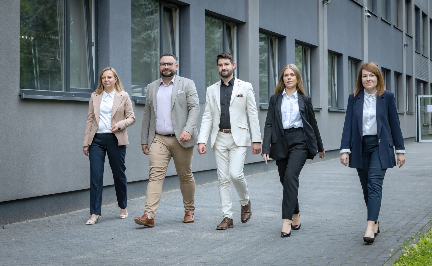 Pięcioro członków zespołu Biznes Medical idzie chodnikiem przed budynkiem biura